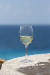 White wine glass against the blue sea. The glass is on a table made of rocks.