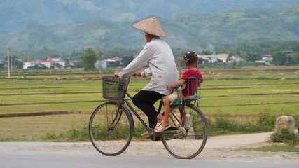 Woman and child cycling through vietnamese valley