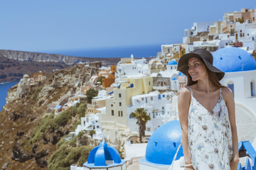 Fototapeta na wymiar A young and attractive woman in a white dress and black hat, walking at the city of Oia, island of Santorini, Greece. Concept - of leisure, tourism, travel, vacations, romance, love.