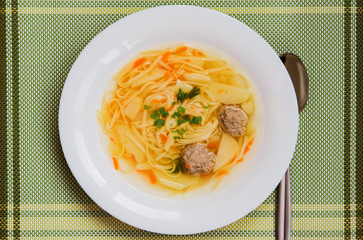 Soup with meatballs, carrots, potatoes and noodles in white bowl on green napkin, top view