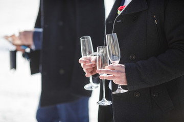 Groom in winter coat holds champagne flutes