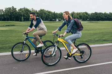 side view of happy couple riding bicycles together in park