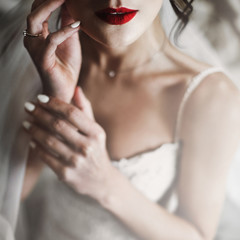 Bride holds her hands before tender red lips