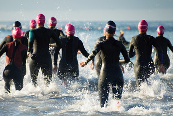 Group triathlon participants running into the water for swim portion of race,splash of water and athletes running