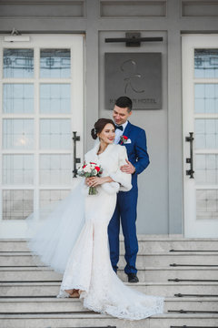 Groom in blue suit and beautiful bride stand outside