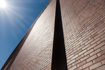 Red brick wall facade against blue sky and sun beams.