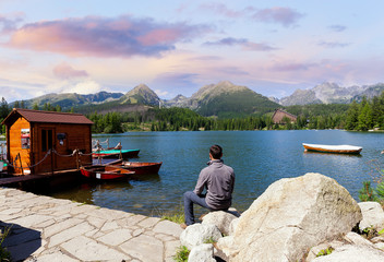 Man sitting on the bank of alpine mountain lake at sunset