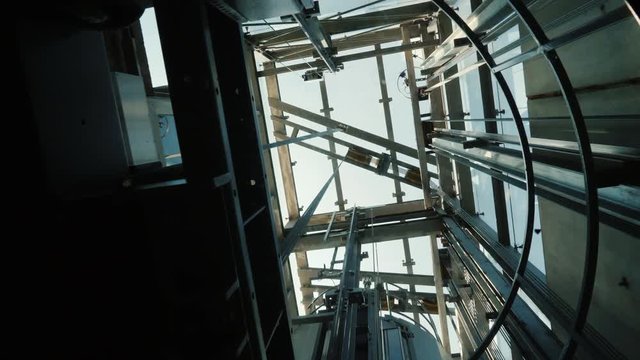 The elevator goes down in the shaft. At the top, you can see the mechanism of the lift, the cables and the blue sky