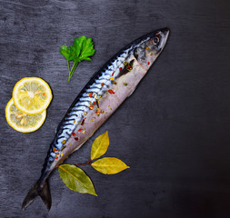 Whole fresh mackerel with spices and lemon on a black background