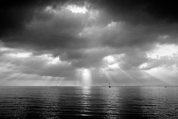 Quiet after storm, sailboat with  sun reflection on  calm waters,dramatic cloudscape in  black and...