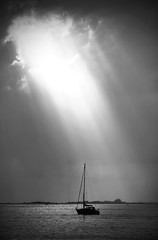 Quiet after storm, sailboat with  sun reflection on  calm waters,dramatic cloudscape in   black and...