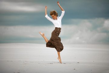Obraz premium Young woman jumps on sand in desert and joyful laughs.