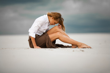 Young sad and pensive woman sits on sand in desert.