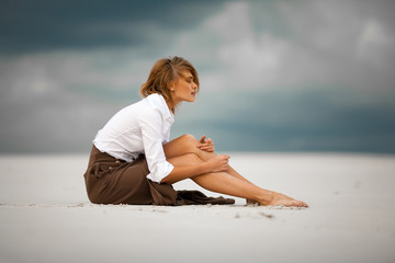 Young sad and pensive woman sits on sand in desert.