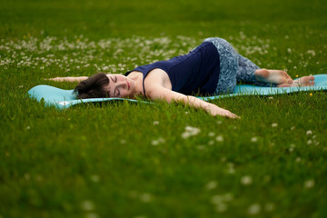 Beautiful caucaisan young woman working out outdoors on blue mat. Jathara Parivartanasana top view