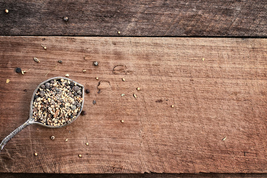 Flatlay image of a tablespoon of pickling spices over a rustic wood plank background. Photo shot from above.