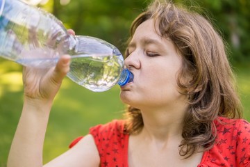 Young woman is drinking water from bottle at sunny hot day.