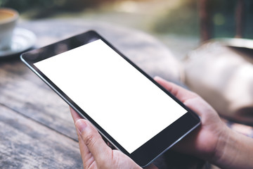Mockup image of woman's hands holding black tablet pc with white blank screen with vintage wooden table background