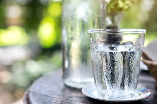 A glass of cold water and bottle on wooden table with blur nature background