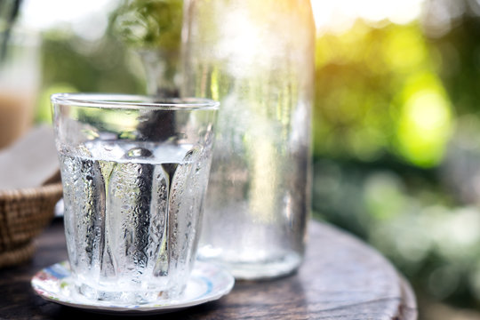 A glass of cold water and bottle on wooden table with blur nature background