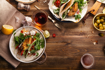 Tacos with fried avocados , tomatoes and greens on distressed wooden background. Served with beer,...