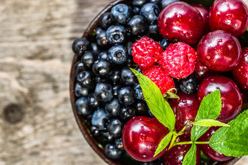 Organic berry fruits in a bowl - cherries, blueberries and raspberries on wooden table