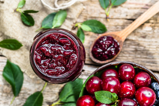 Homemade jam from cherry preserved in jar and fresh cherries in a bowl