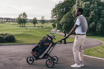 Smiling african american man in sunglasses walking with bag full of golf clubs