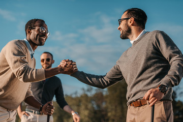 Happy stylish multicultural friends shaking hands while playing golf on golf course