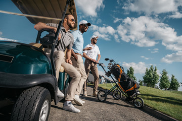 group of smiling friends standing near golf cart and looking away - Powered by Adobe