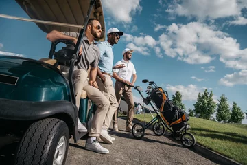 Fotobehang group of smiling friends standing near golf cart and looking away © LIGHTFIELD STUDIOS