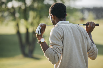 rear view of african american man holding golf club and looking away