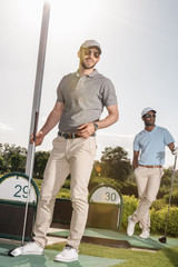 Fototapeta na wymiar stylish players with golf clubs in hands standing at golf course