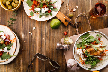 Tacos with fried avocados , tomatoes and greens on distressed wooden background. Served with beer, lime and olives. Mexican cuisine interpretation. Horizontal composition with copy space.