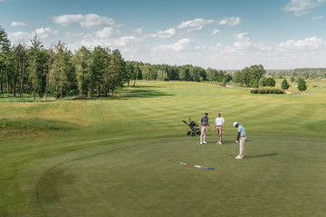 Fototapeta na wymiar multiethnic group of sportsmen playing golf on green fairway at daytime