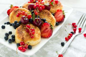 Healthy breakfast: cheese pancakes with sour cream and fresh ripe berries on white wooden table. Selective focus 