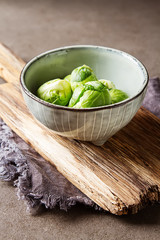 Fresh Brussels sprouts in a ceramic bowl. Wooden plank. Dark gray background.