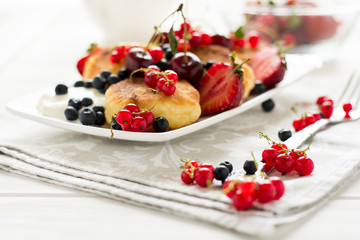 Healthy breakfast: cheese pancakes with sour cream and fresh ripe berries on white wooden table. Selective focus 
