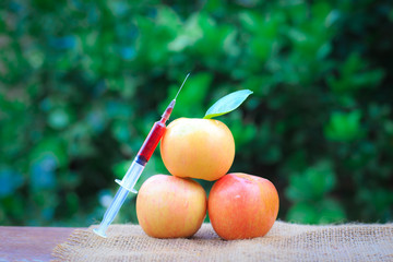 Needle and syringe injected in the apple, Enhanced fruits. Nutrition concept, GMO concept. Background of nature.