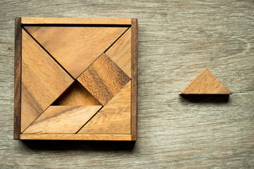 Tangram puzzle in square shape with box wait for fulfillment with one triangle piece on wooden background