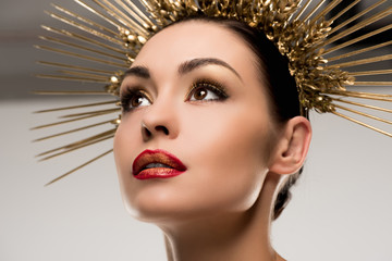 glamorous woman with makeup wearing golden headpiece isolated on grey