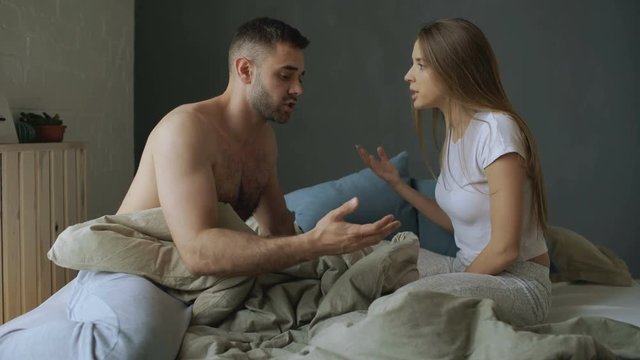 Upset young couple in sitting in bed quarrelling and argue each other. Woman punch her boyfriend and go away