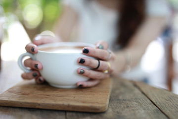 Beautiful hipster woman touch a coffee cup at cafe while drinking coffee, Relaxing holiday concept. Selective focus a cup.