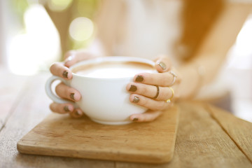 Beautiful hipster woman touch a coffee cup at cafe while drinking coffee, Relaxing holiday concept. Selective focus a cup.