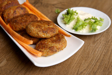 Fish cutlets with carrots and mayonnaise sauce. Homemade fried  cutlets in plate on wooden table.
