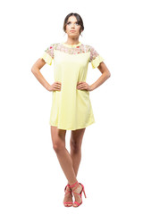 Gorgeous young woman in yellow short dress with arms on hips looking up thoughtful. Full body length portrait isolated on white background. 