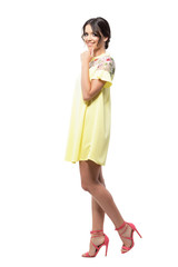 Gorgeous cute woman in yellow dress smiling at camera with hands on chin. Full body length portrait isolated on white background. 