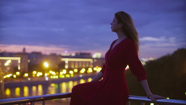 Young woman in red dress is sitting on a parapet