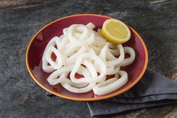 White seafood. Squid rings with lemon on a ceramic plate. Dark background.