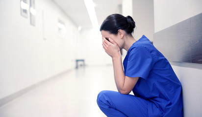 sad or crying female nurse at hospital corridor